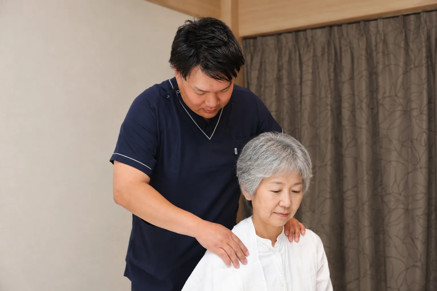 椅子に座ったご利用者の肩をやさしくマッサージする院長