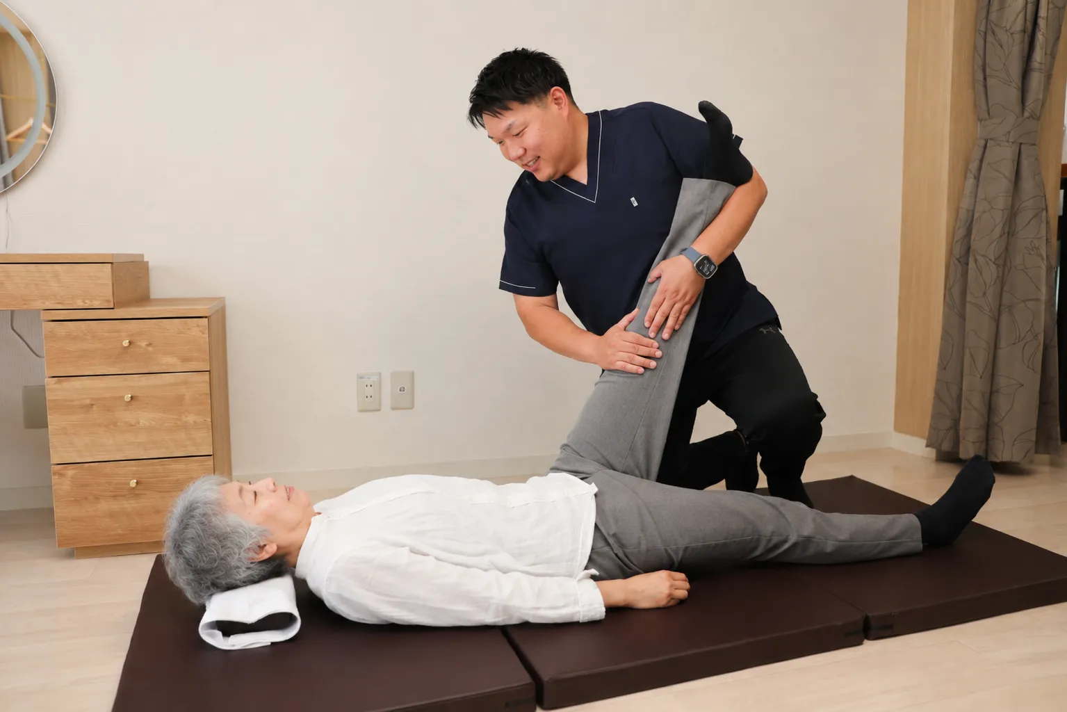 床に横たわるご利用者の脚をやさしく支えながらストレッチする院長